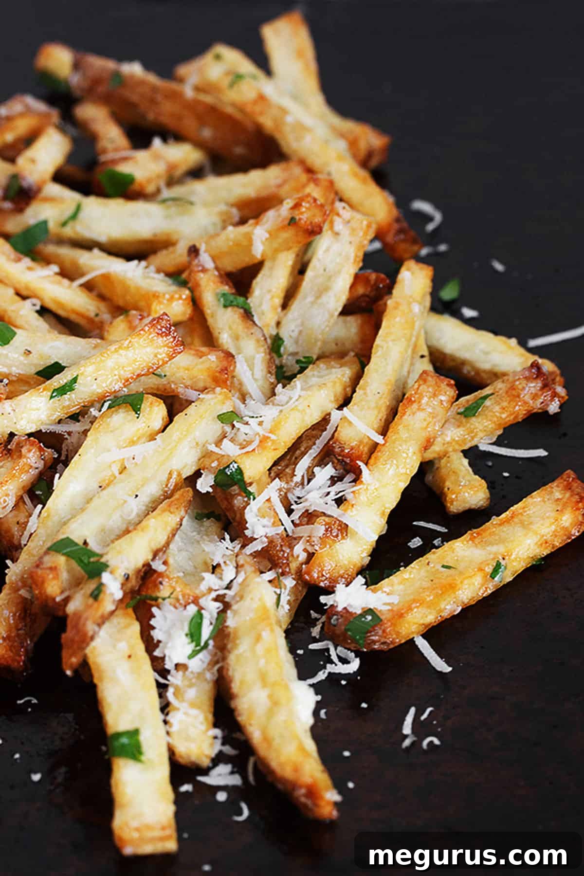 Close-up shot of golden-brown fries being tossed with a generous amount of creamy garlic aioli and sprinkled with freshly grated Parmesan cheese, ready to serve.