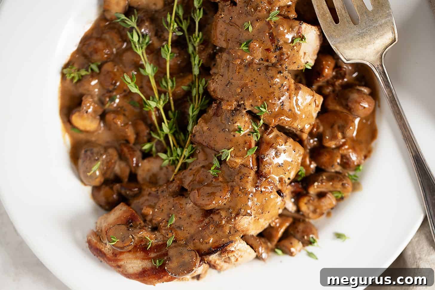 Perfectly cooked pork Diane medallions on a serving plate, generously topped with a rich, creamy mushroom sauce and garnished with fresh herbs.