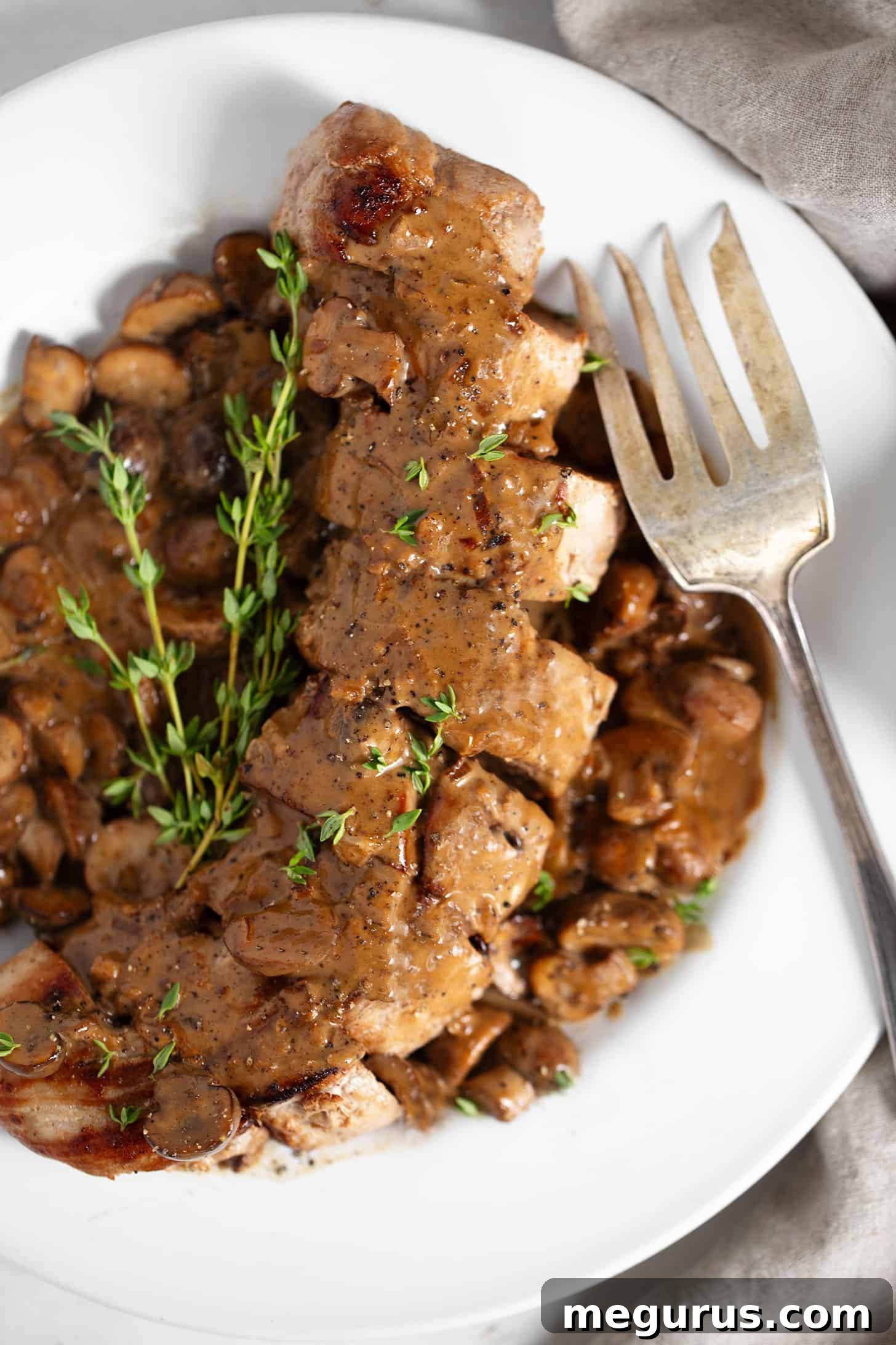 A close-up of a serving of Pork Diane on a white plate, with a fork ready to enjoy the tender pork and creamy mushroom sauce.