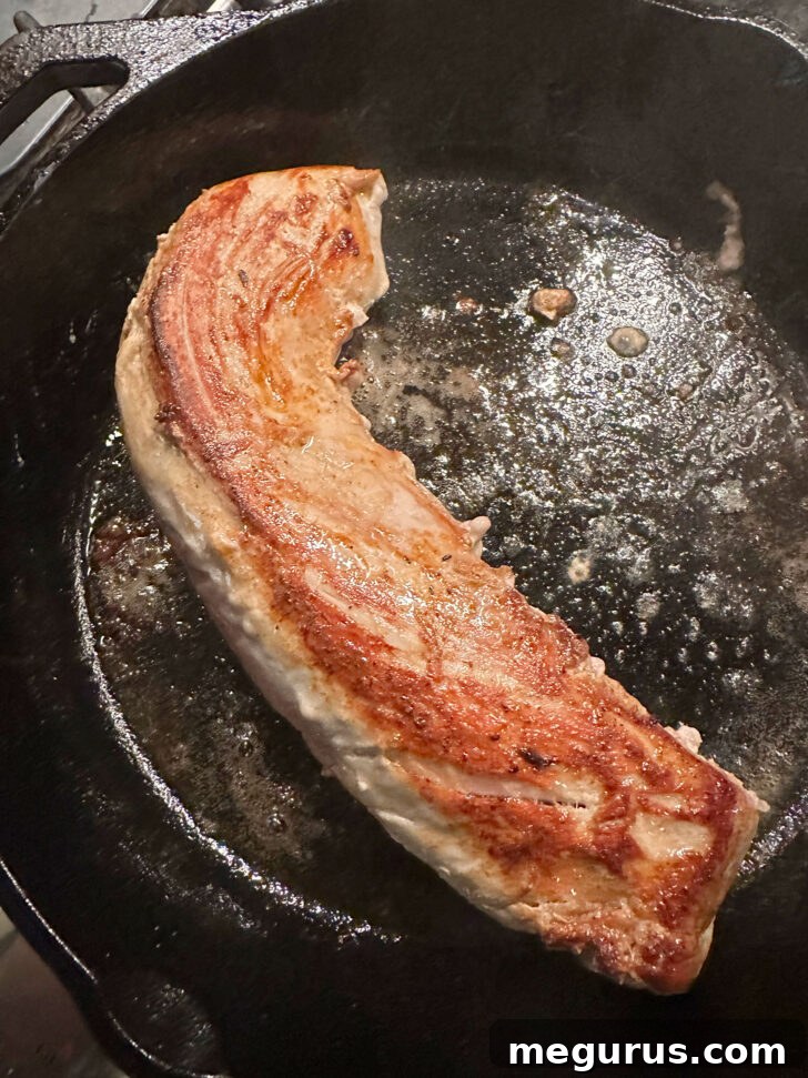 Pork tenderloin being browned in a skillet, creating a delicious crust.