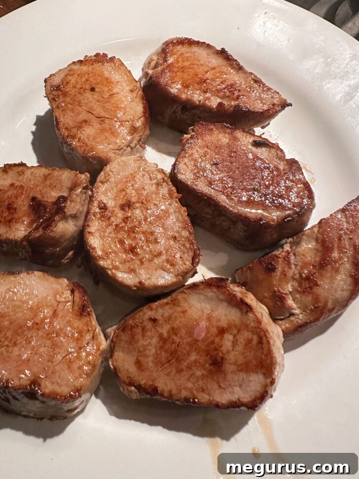 Cooked pork medallions transferred to a plate and loosely tented with foil to keep warm while the sauce is prepared.