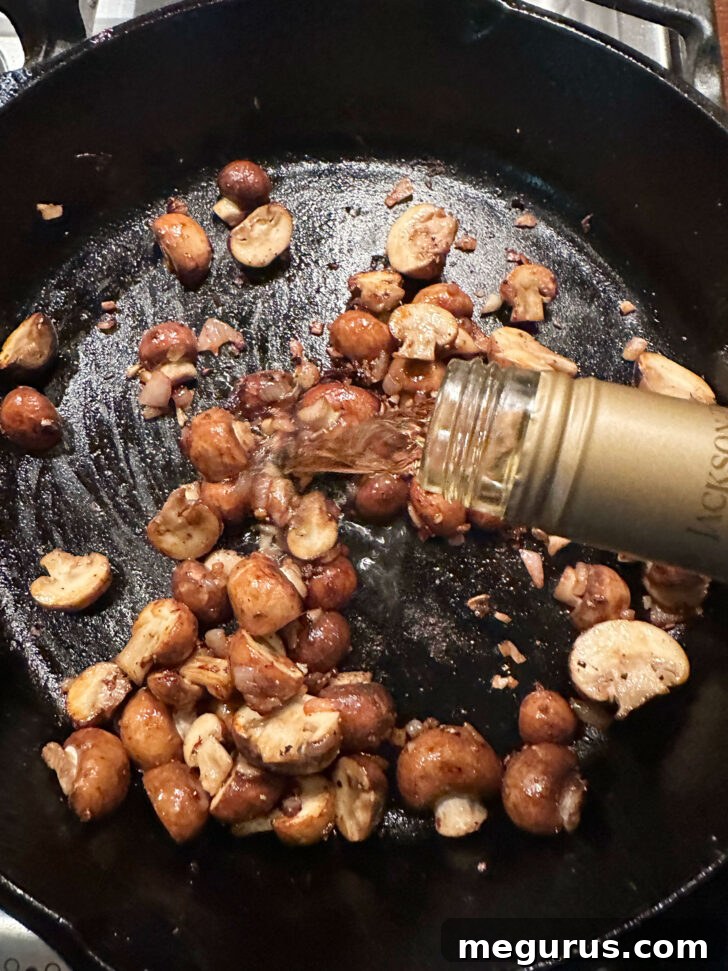 White wine being poured into the skillet with browned mushrooms, beginning the deglazing process.