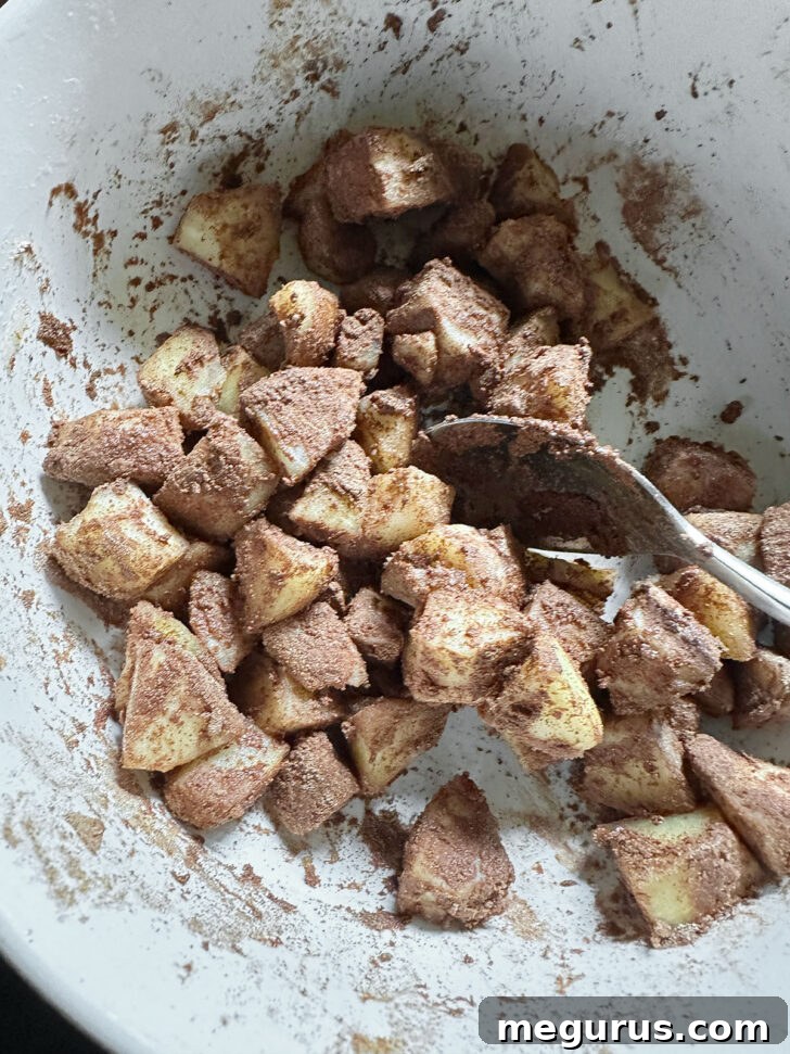 Cinnamon sugar mixture thoroughly stirred into the softened apple chunks in a bowl, creating the topping.