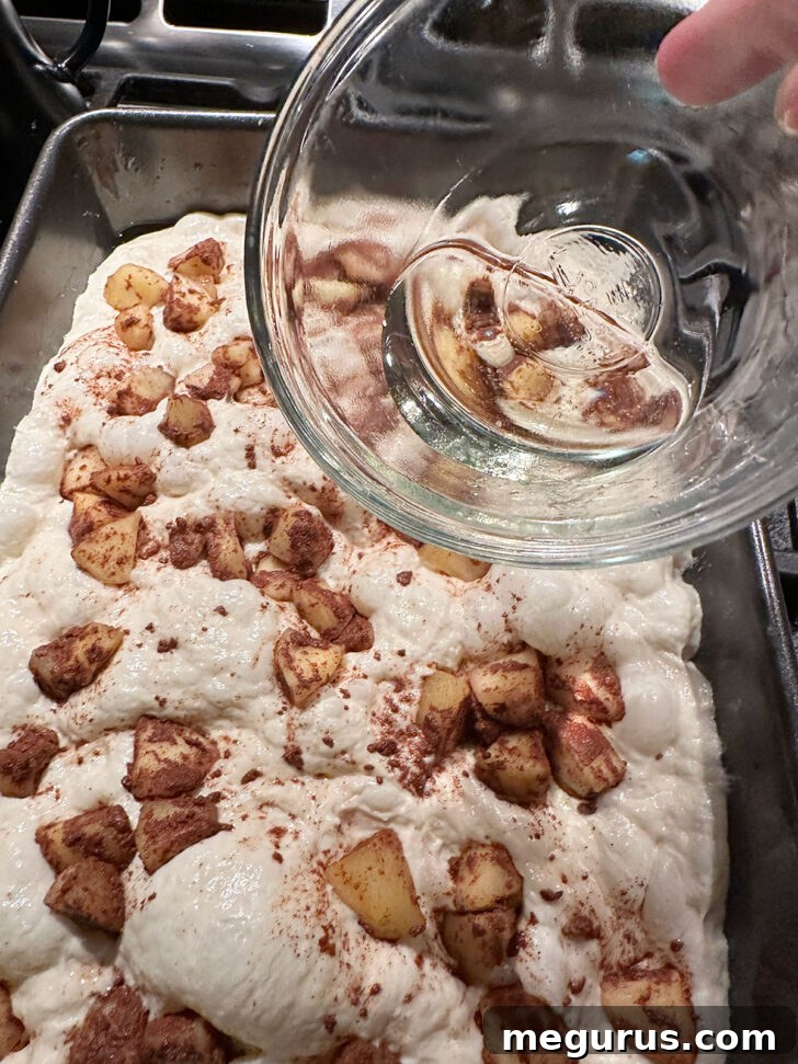 Cinnamon apple mixture scattered over the risen focaccia dough, with dimples visible where apples are pressed in.