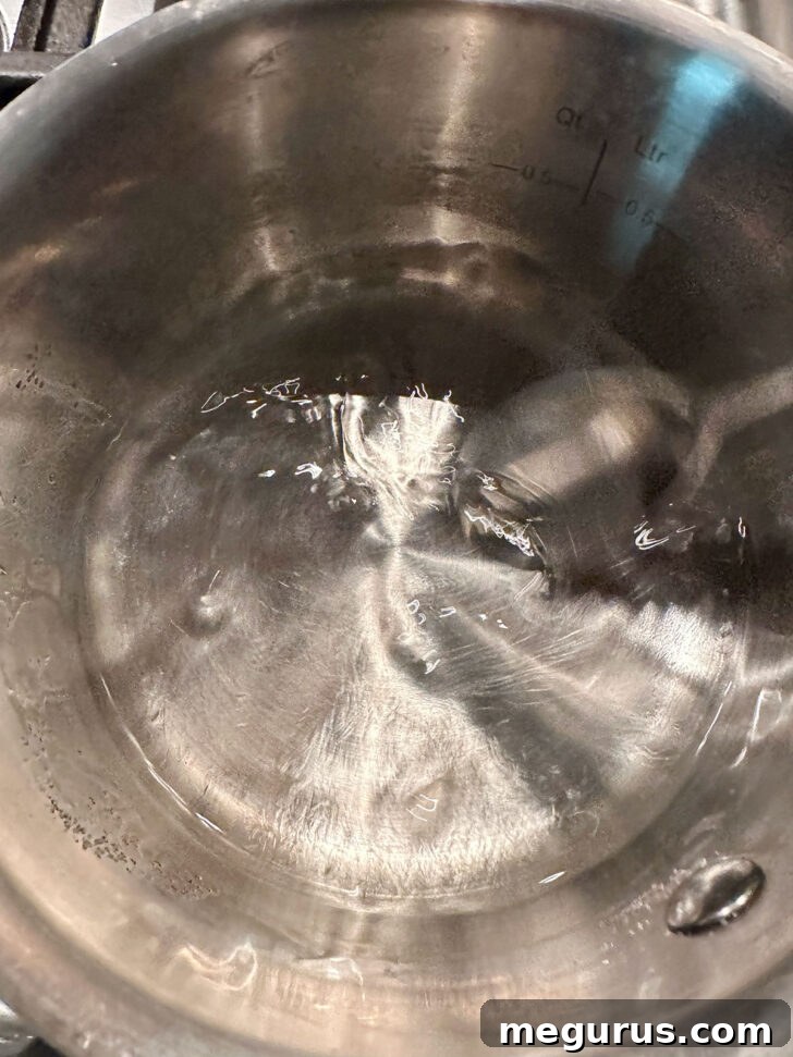 Water, sugar, and corn syrup boiling in a small saucepan, creating the base for the fritter glaze.