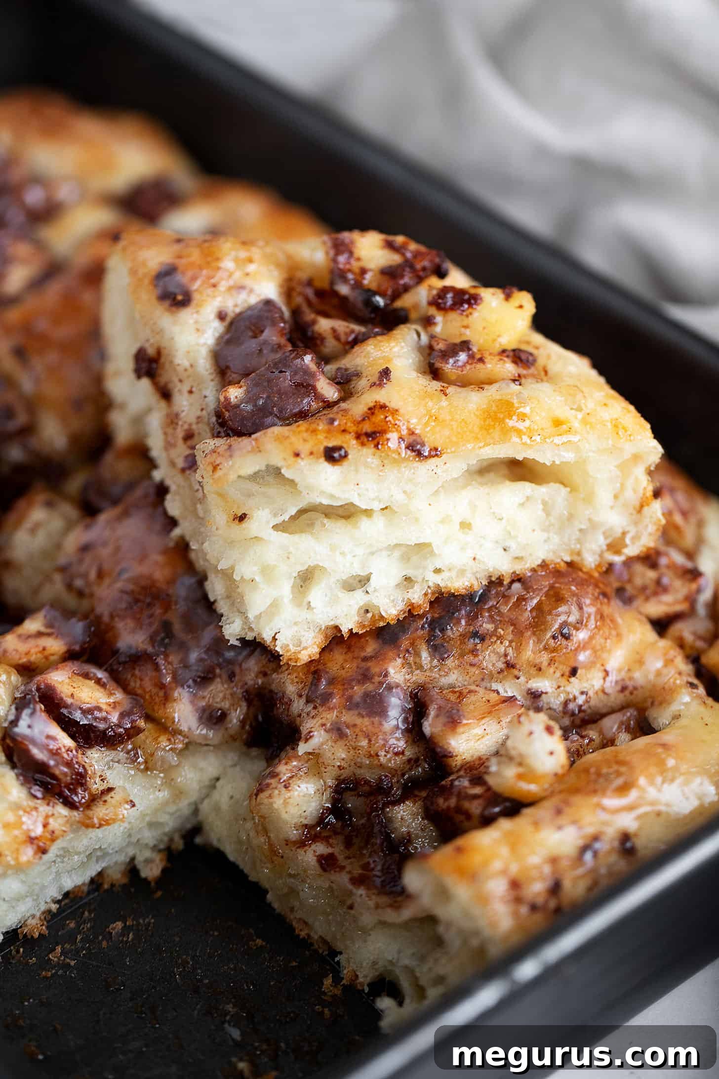 A close-up of the freshly glazed Apple Fritter Focaccia in the baking pan, showing the shiny glaze and apple pieces embedded in the soft bread.