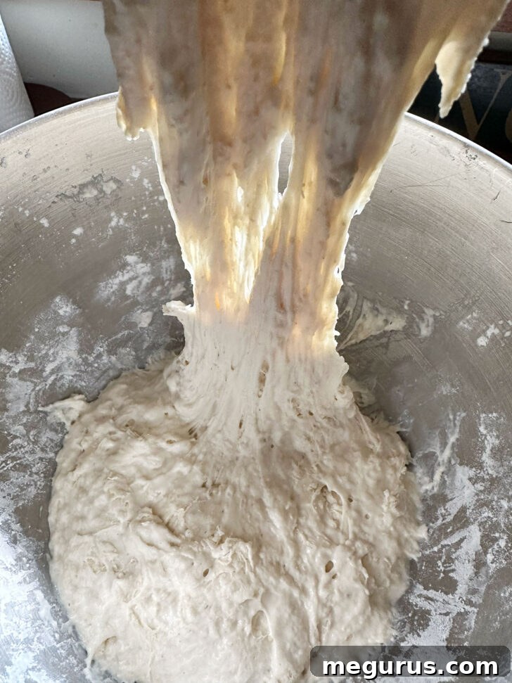 A hand gently stretching and folding the wet focaccia dough in a mixing bowl, demonstrating the no-knead technique.