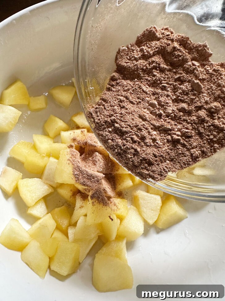 Cooked apples in a bowl with cinnamon sugar being sprinkled over them, ready to be mixed.