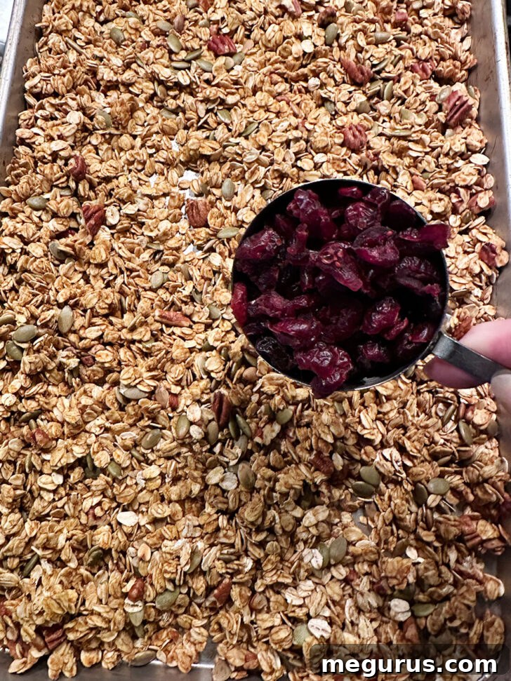 Adding dried cranberries to pumpkin granola after baking.