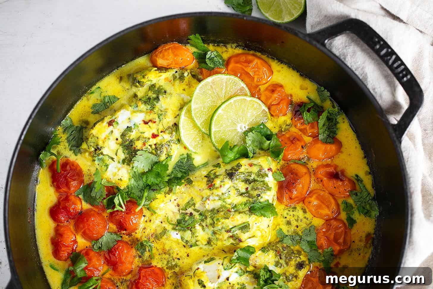 Golden-hued coconut milk fish baking in a pan with roasted cherry tomatoes.