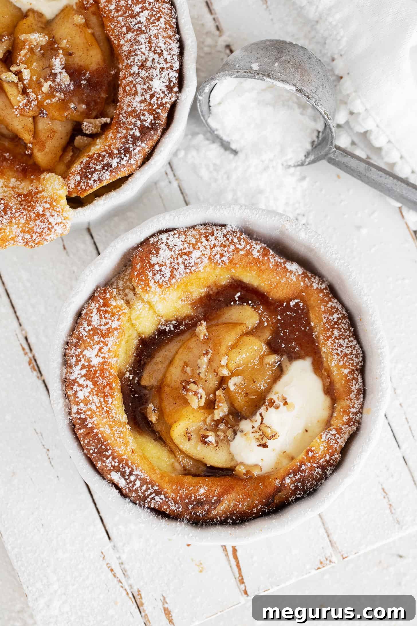 Individual apple dutch babies on serving board, garnished with nuts and powdered sugar.