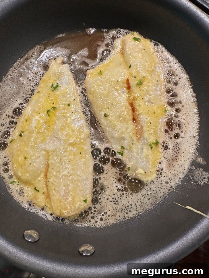 Sole fillets being pan-fried in a skillet with melted butter and olive oil.