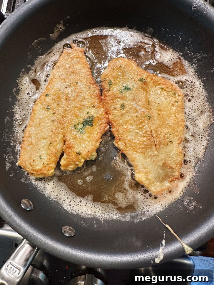 Pan-fried sole fillets golden brown on one side, just flipped in the skillet.