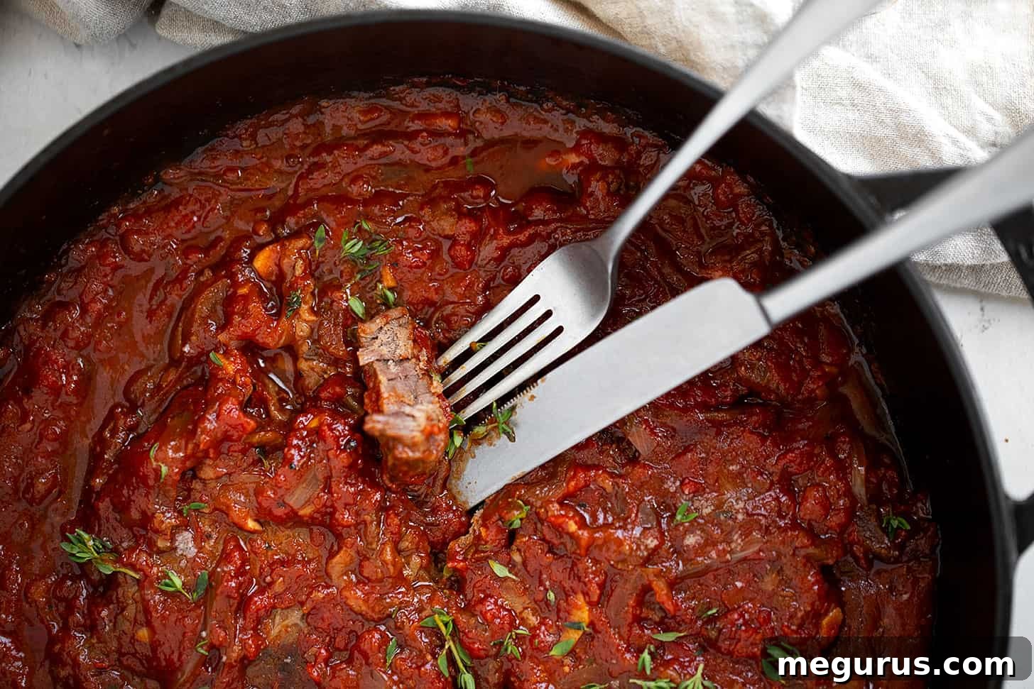 Swiss steak in skillet with fork and knife.