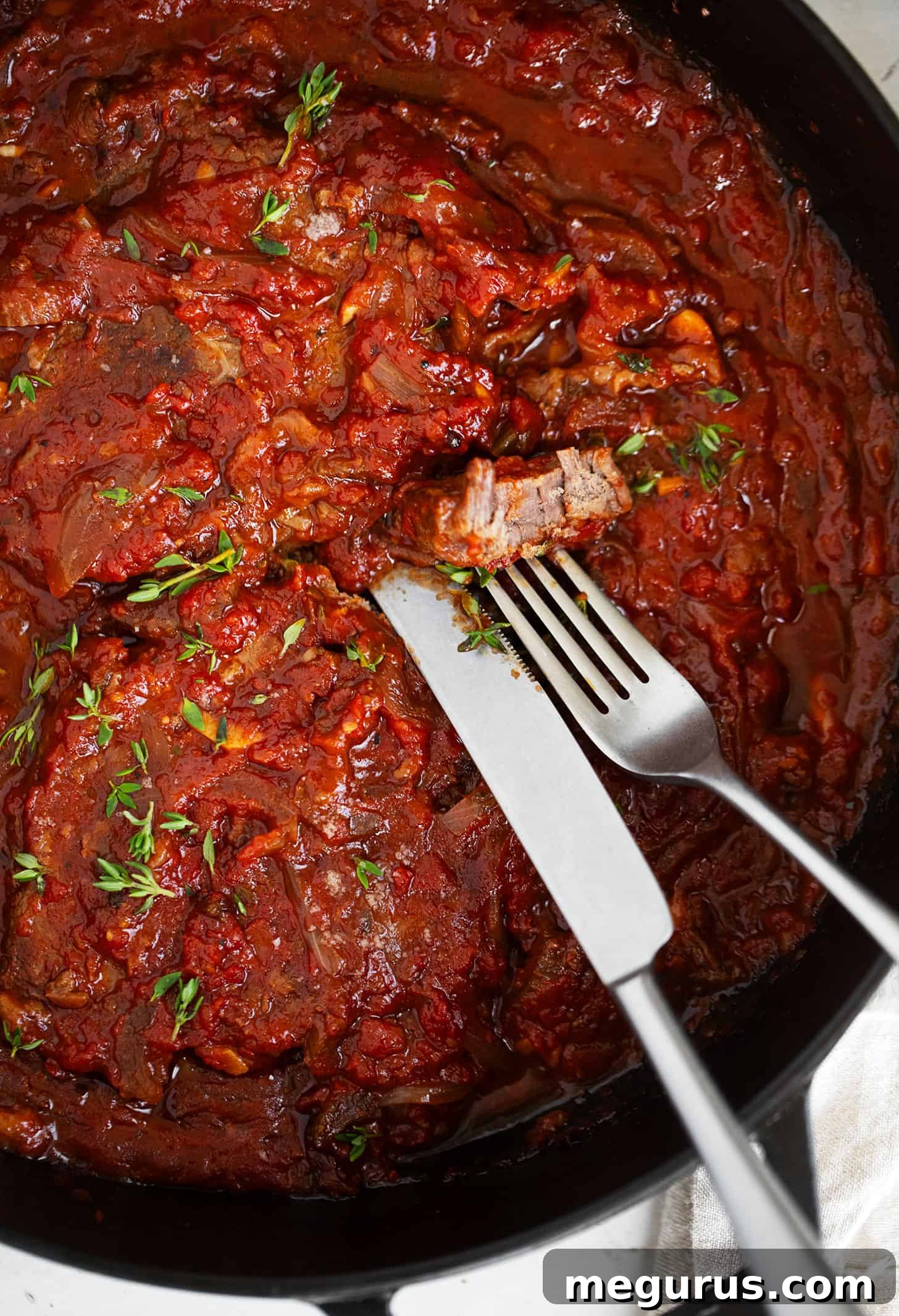 Swiss steak in pan with a knife and fork.