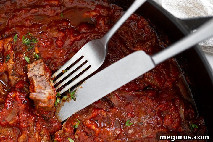 Swiss steak in skillet with fork and knife.