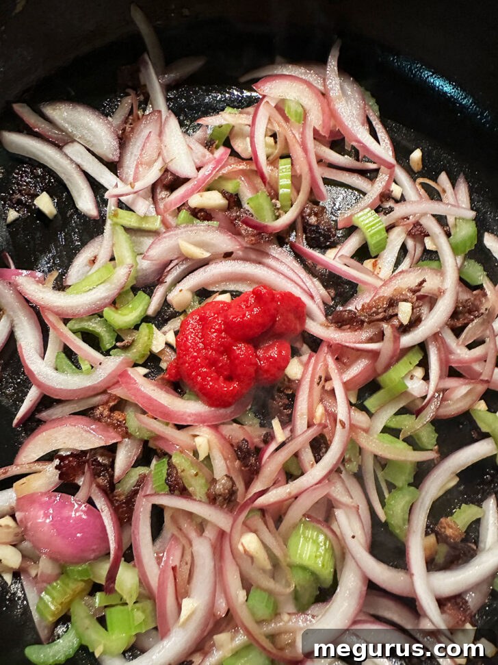Adding tomato paste to the skillet.