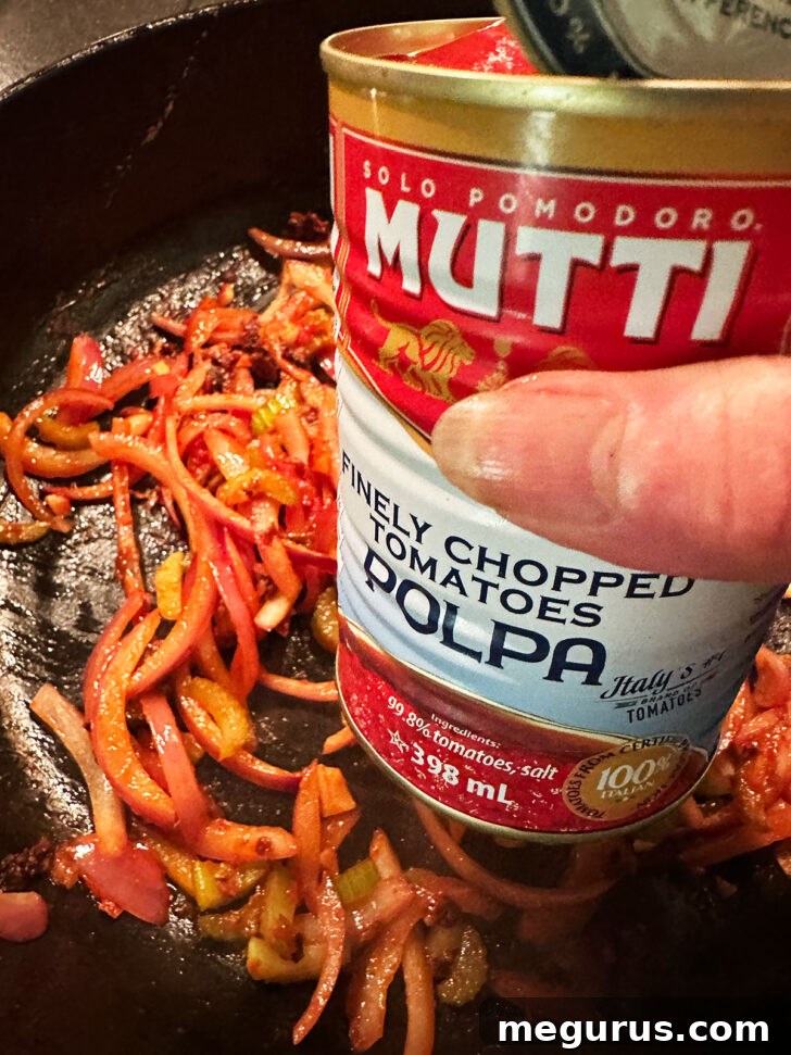 Adding the canned tomatoes to the skillet.