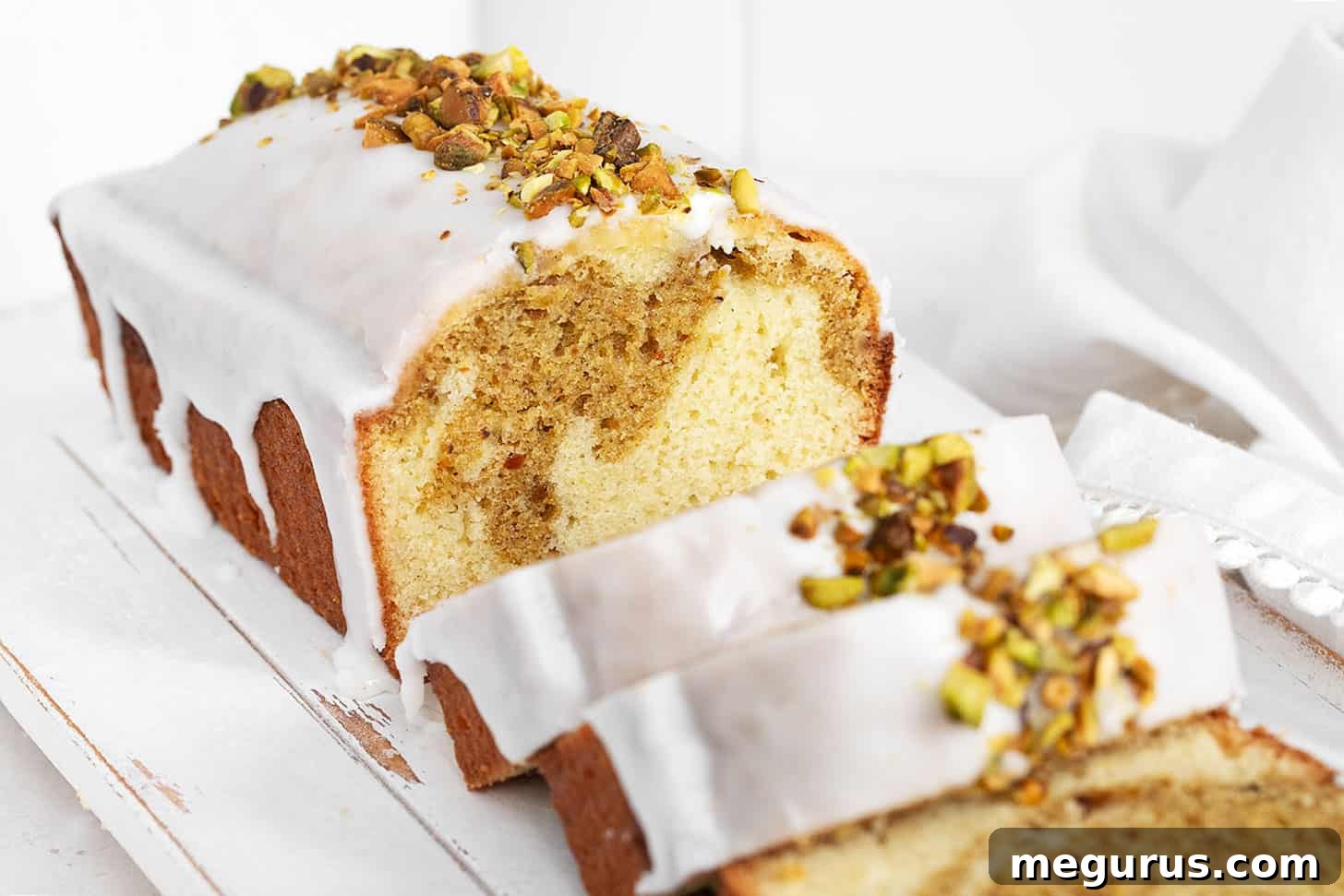 A beautifully sliced Lemon Pistachio Loaf Cake, revealing its vibrant green pistachio swirl and glossy lemon glaze, adorned with chopped pistachios on a rustic serving board.
