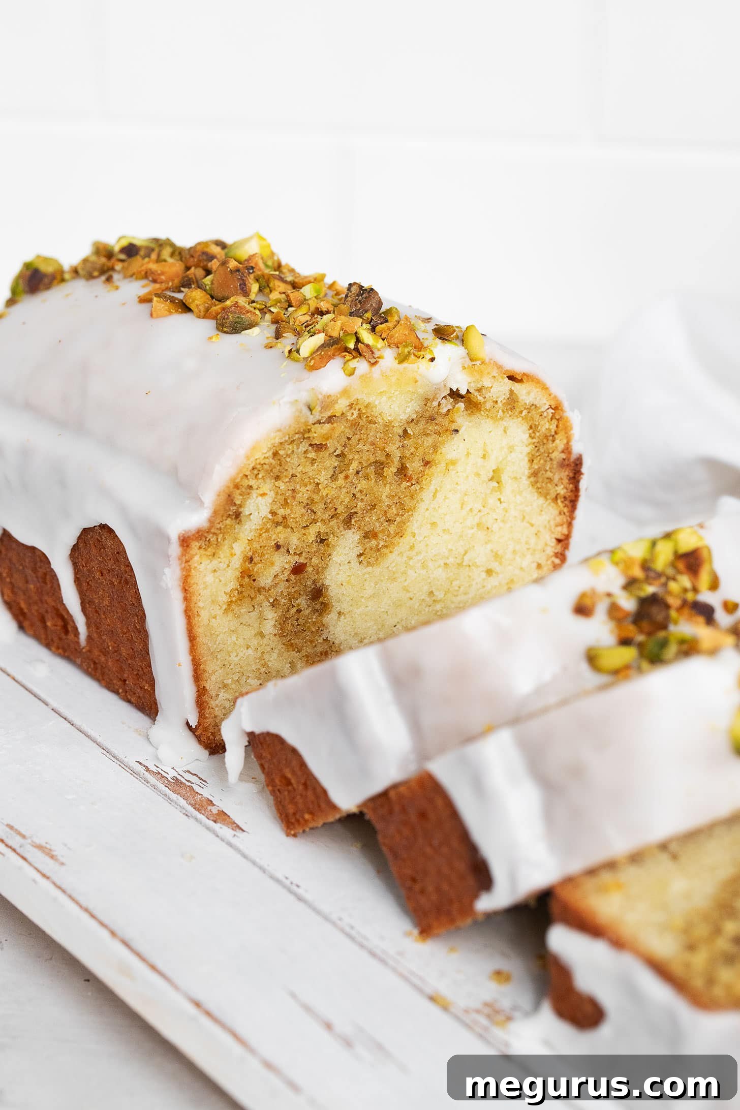 A large, perfectly baked and sliced Lemon Pistachio Loaf Cake with glaze and pistachios, presented on a wooden board, ready for serving.
