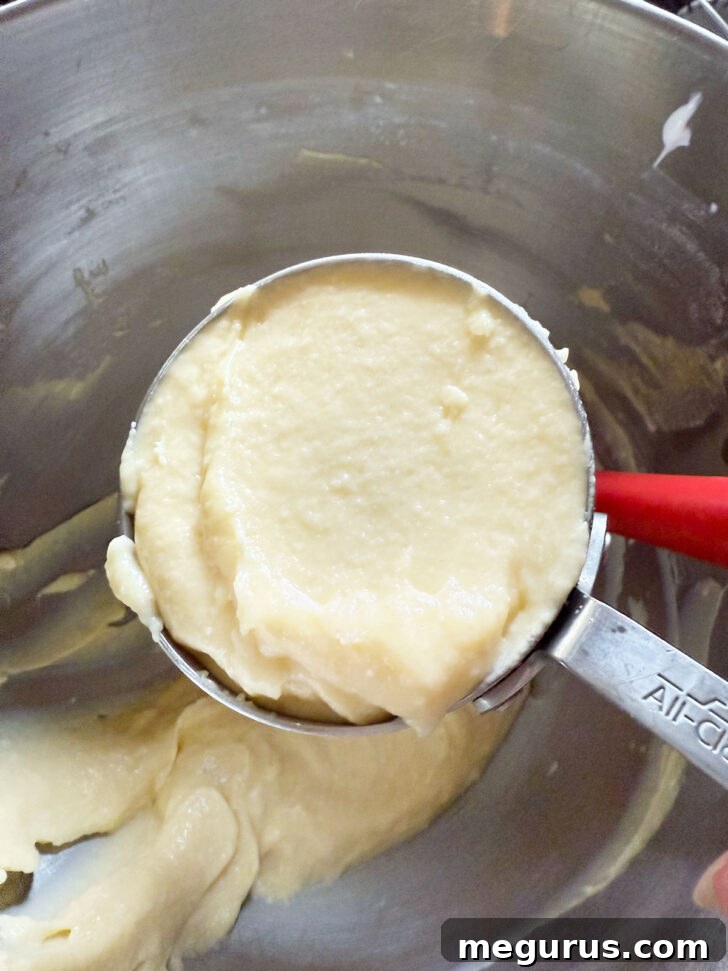 One cup of the plain cake batter being scooped out into a separate bowl, to be flavoured with pistachio.