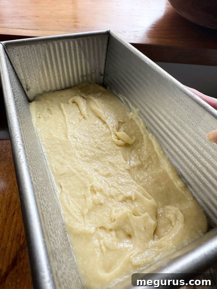 A thin, even layer of the plain cake batter spread across the bottom of the prepared loaf pan.