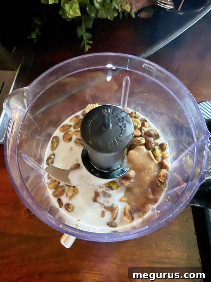 Shelled pistachios, brown sugar, and milk loaded into a food processor, ready for blending into a smooth paste.