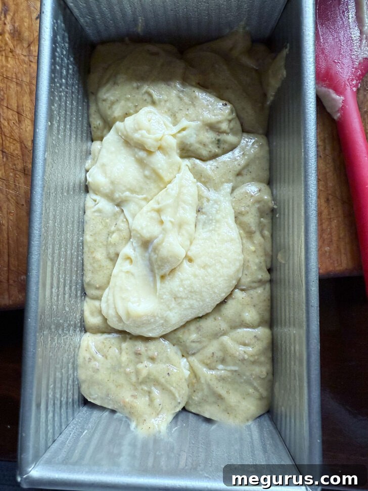 Alternating dollops of plain and pistachio-swirled batter being carefully dropped into the prepared loaf pan.