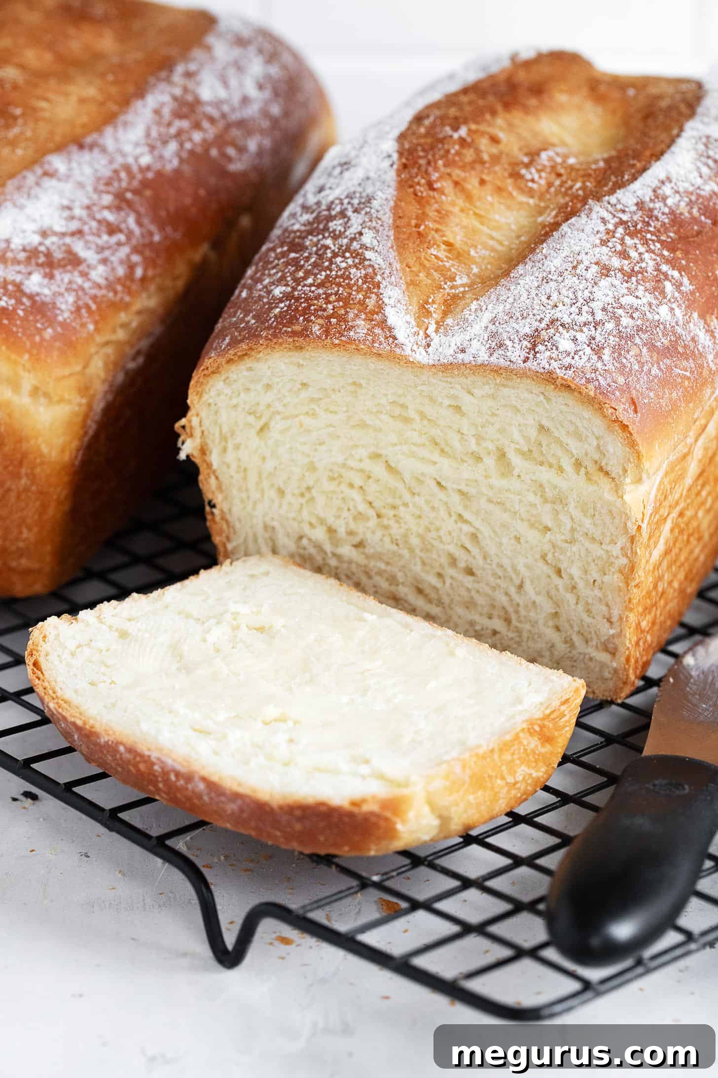 Two slices of homemade overnight sandwich bread, one with butter, on a cooling rack.