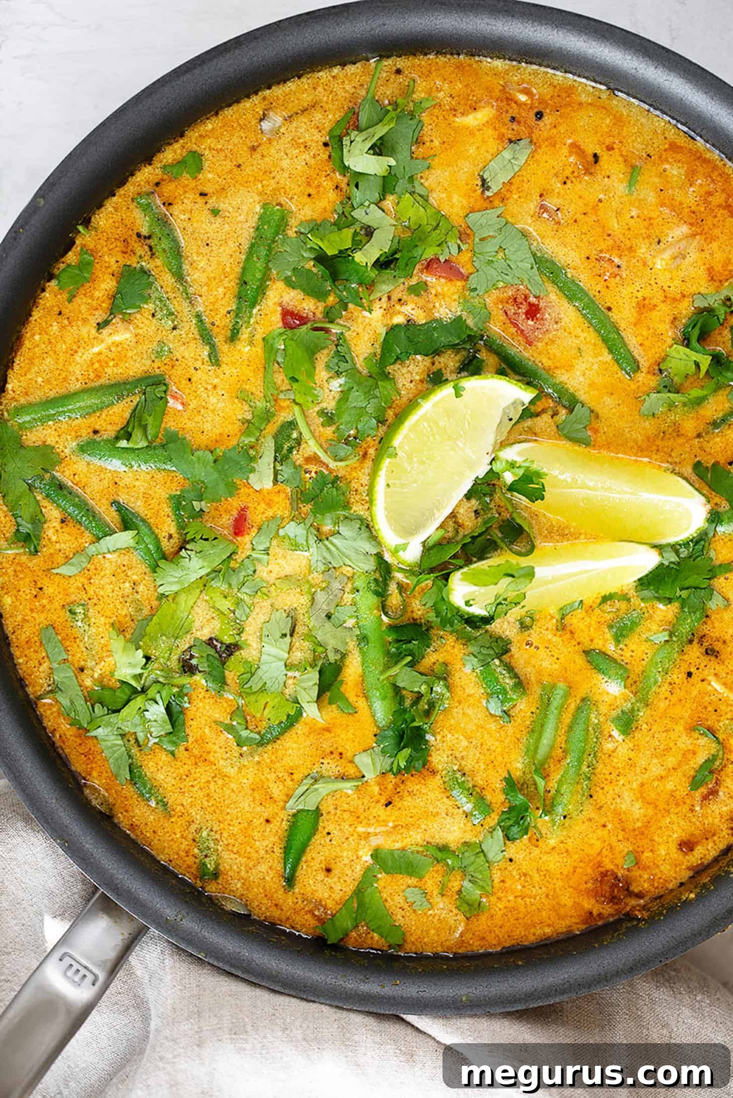 Close-up of creamy chicken peanut butter curry garnished with fresh lime slices and cilantro in a large skillet.