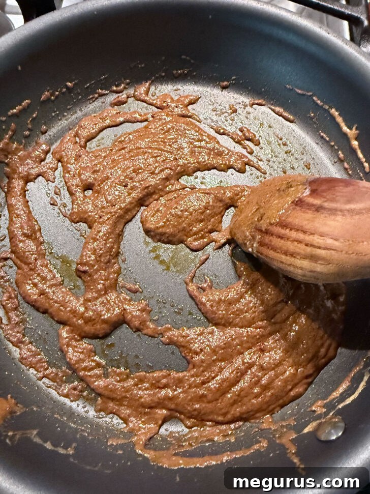 Curry paste and coconut cream mixture sizzling gently in a skillet, stirred to release aromas.