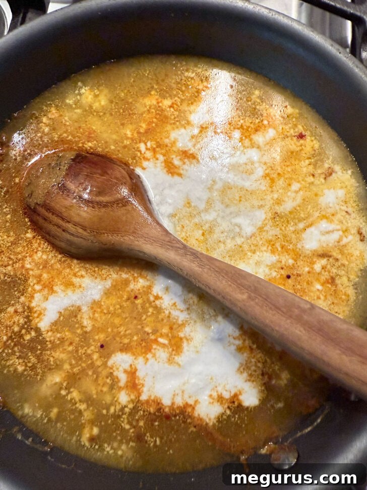 Chicken broth and the remaining coconut milk being poured into the skillet with the curry paste mixture.