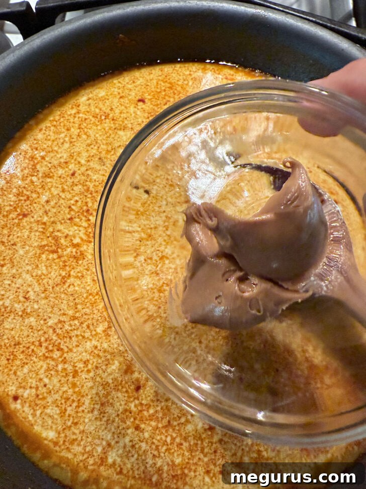 Creamy peanut butter being stirred into the simmering curry sauce in a skillet.