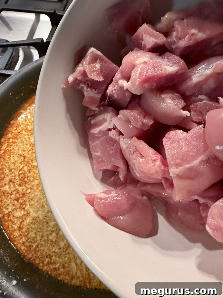 Uncooked chicken pieces added to the simmering peanut butter curry sauce.
