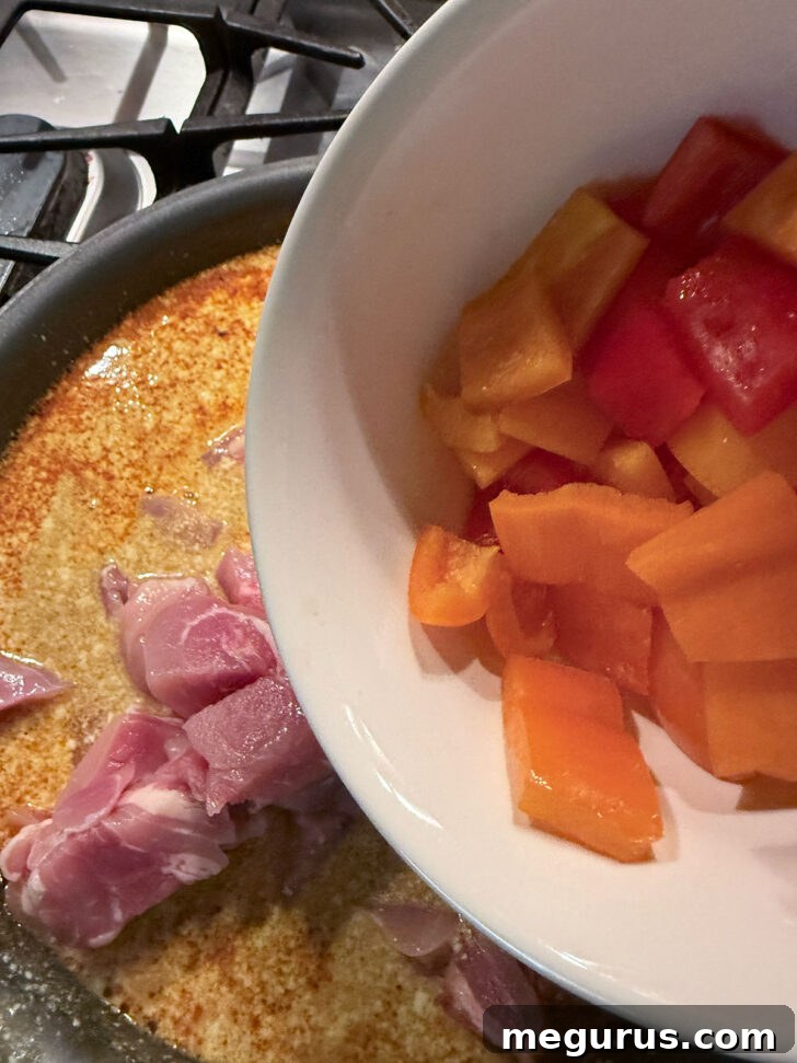 Chopped bell peppers added to the skillet with chicken and curry sauce.