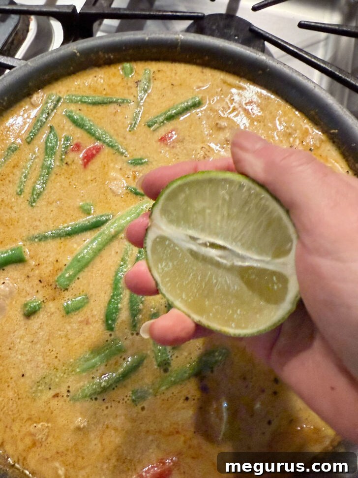 Fresh lime juice being squeezed directly into the finished chicken peanut butter curry for brightness.
