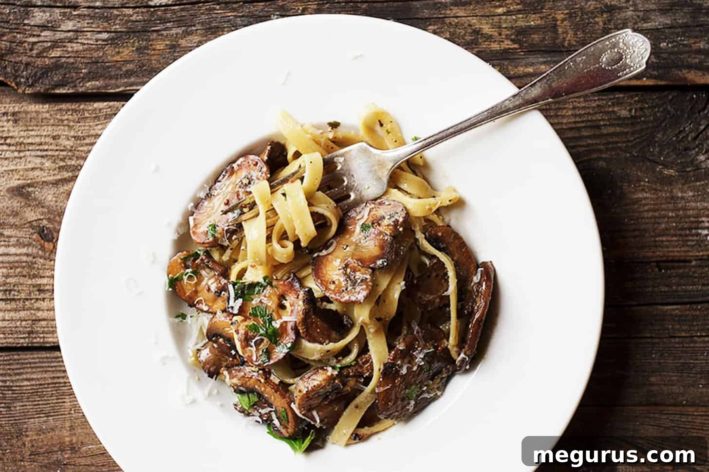 A close-up of creamy mustard pasta with golden mushrooms in a white bowl, ready to be enjoyed with a fork.