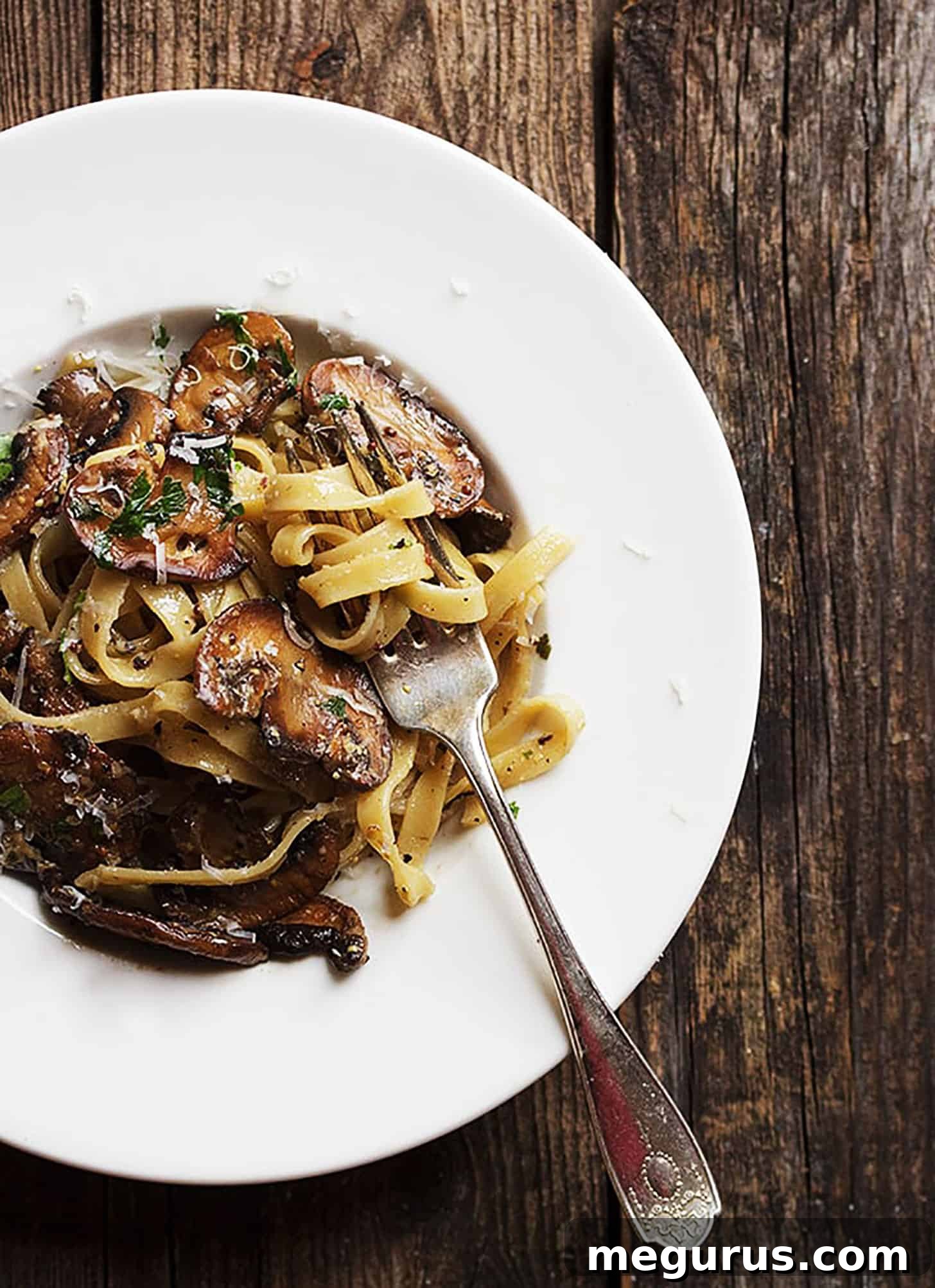 A close-up of the creamy mustard sauce coating the pasta and mushrooms in a white bowl, garnished with fresh parsley.