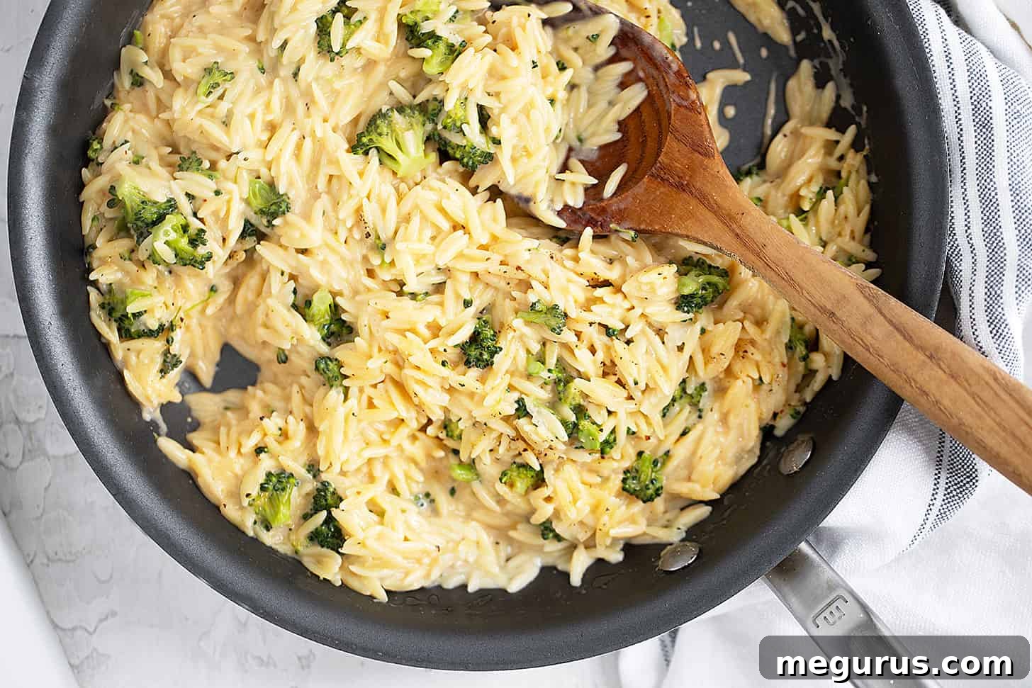 Broccoli cheddar orzo in skillet with a wooden spoon, ready to be served.