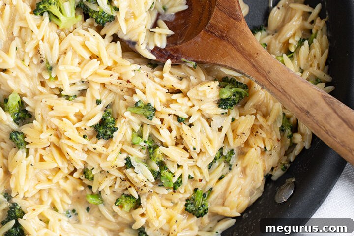 Broccoli cheddar orzo in skillet with a wooden spoon.