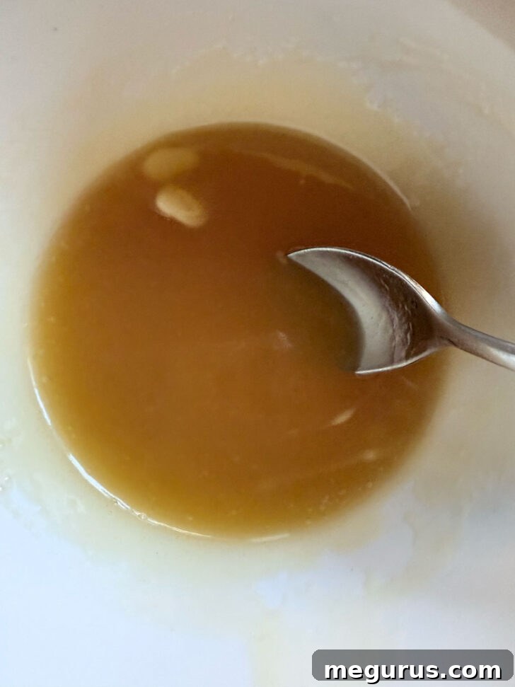 Melted honey butter mixture in a bowl with a spoon, showing its golden color.