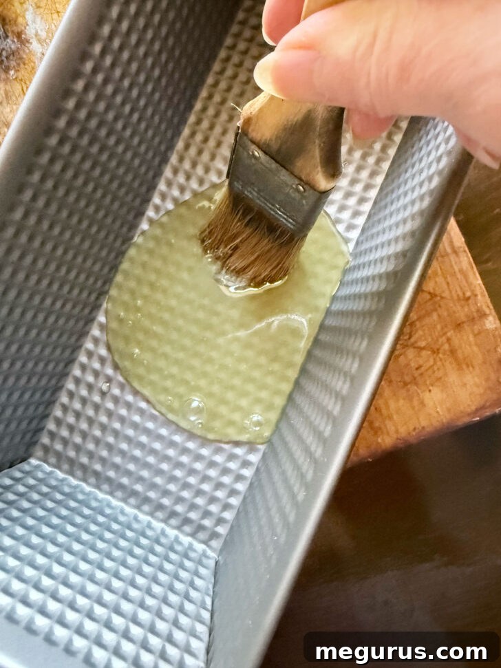 A pastry brush applying honey butter to the bottom and sides of a loaf pan.