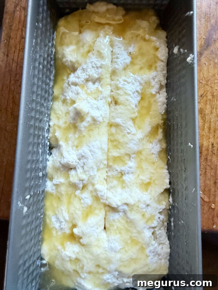 A bench scraper making a lengthwise slash in the raw dough in the loaf pan.