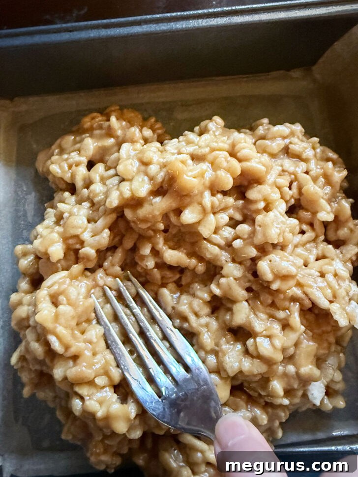 Pressing the rice krispie mixture into a parchment-lined pan.