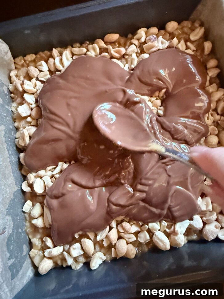 Spreading melted chocolate mixture over the peanuts in the pan.