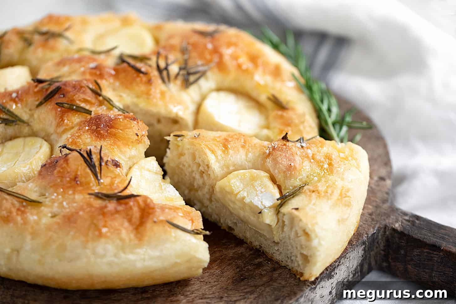 Golden-brown mini Brie focaccia, elegantly sliced and arranged on a rustic cutting board, showcasing melted cheese and fresh rosemary.