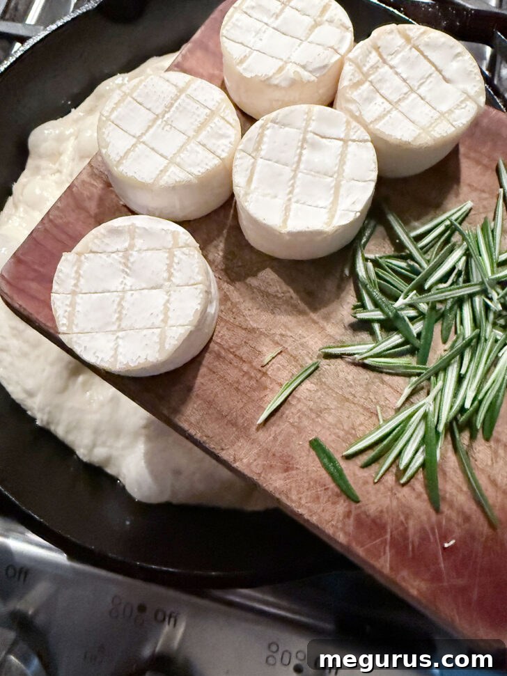 Mini Brie rounds and fresh rosemary leaves placed on top of dimpled focaccia dough.