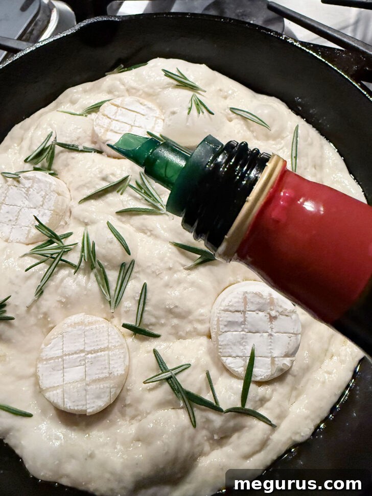 A hand drizzling olive oil over the focaccia dough before it goes into the oven.