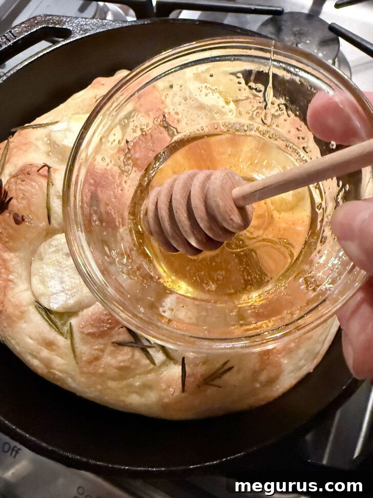 A baked focaccia being drizzled generously with honey while still hot.