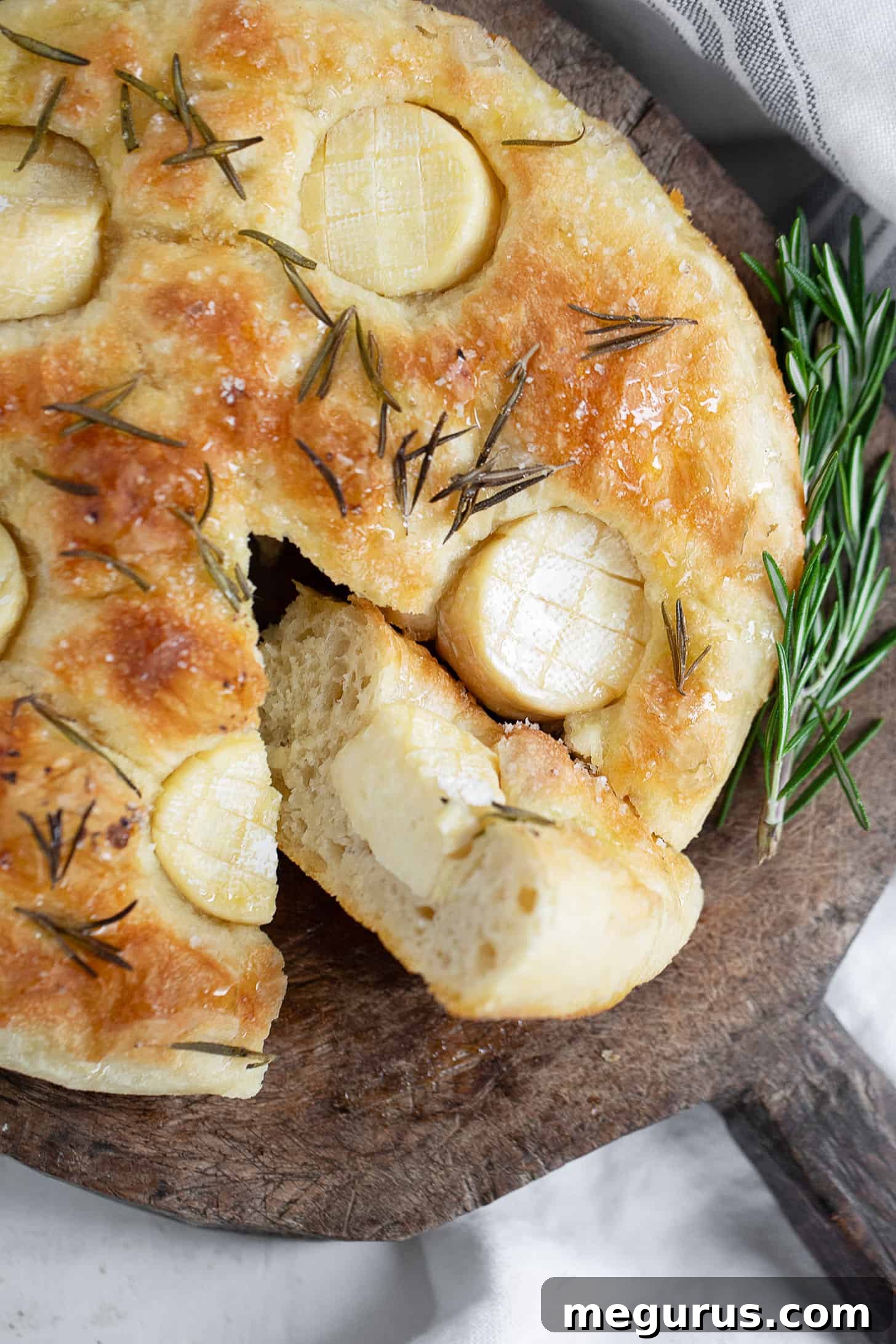 Close-up of a beautifully baked and sliced mini Brie focaccia on a wooden cutting board.